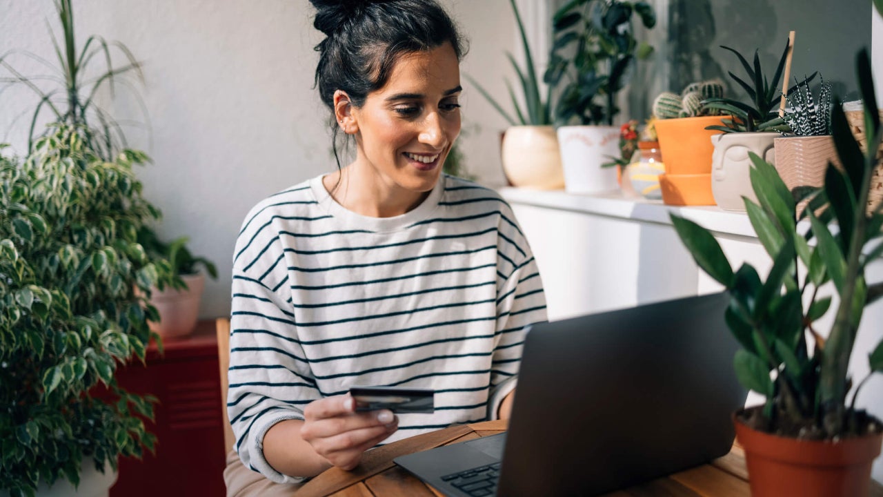 Young woman uses credit card and laptop at kitchen table