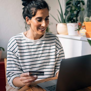 Young woman uses credit card and laptop at kitchen table