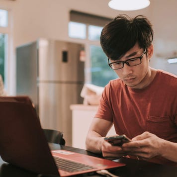 Young man works at kitchen table with laptop and smartphone