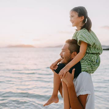 Father carrying young daughter on shoulders on beach at sunset