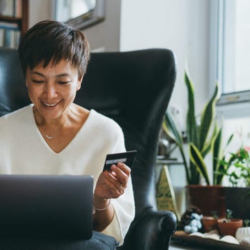 Smiling senior woman holds her credit card and uses her laptop in her home office