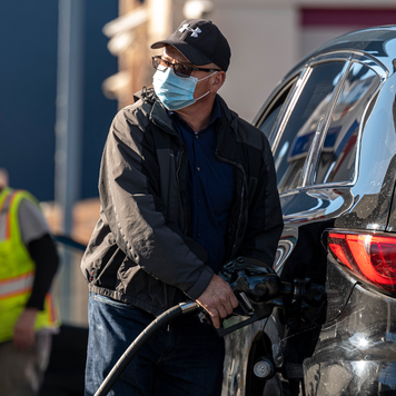 A person wearing a protective mask holds a fuel pump nozzle at a Chevron Corp. gas station in San Francisco, California.