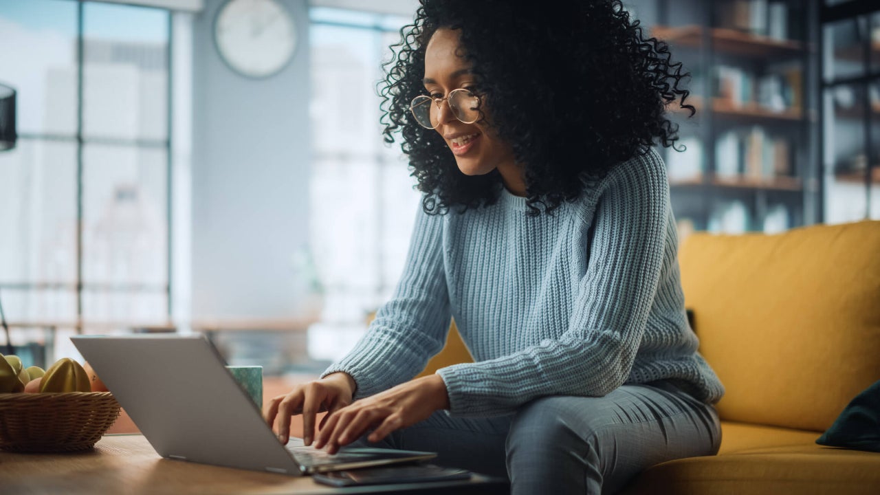 Young woman in her living room smiling and using her laptop