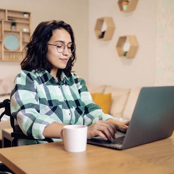 Young woman in a wheelchair uses her laptop in her bedroom at a desk