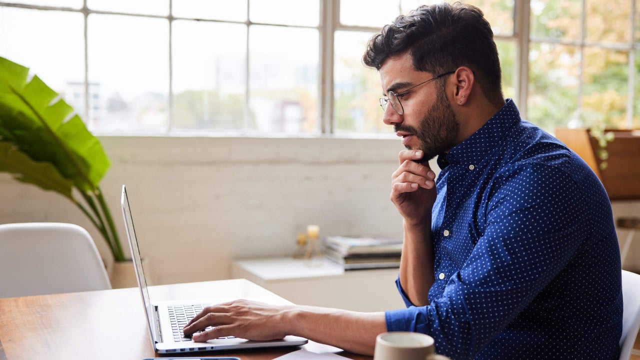 Young man using a laptop with a deep-in-thought expression