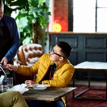 Man paying for lunch at restaurant table with waiter and friend