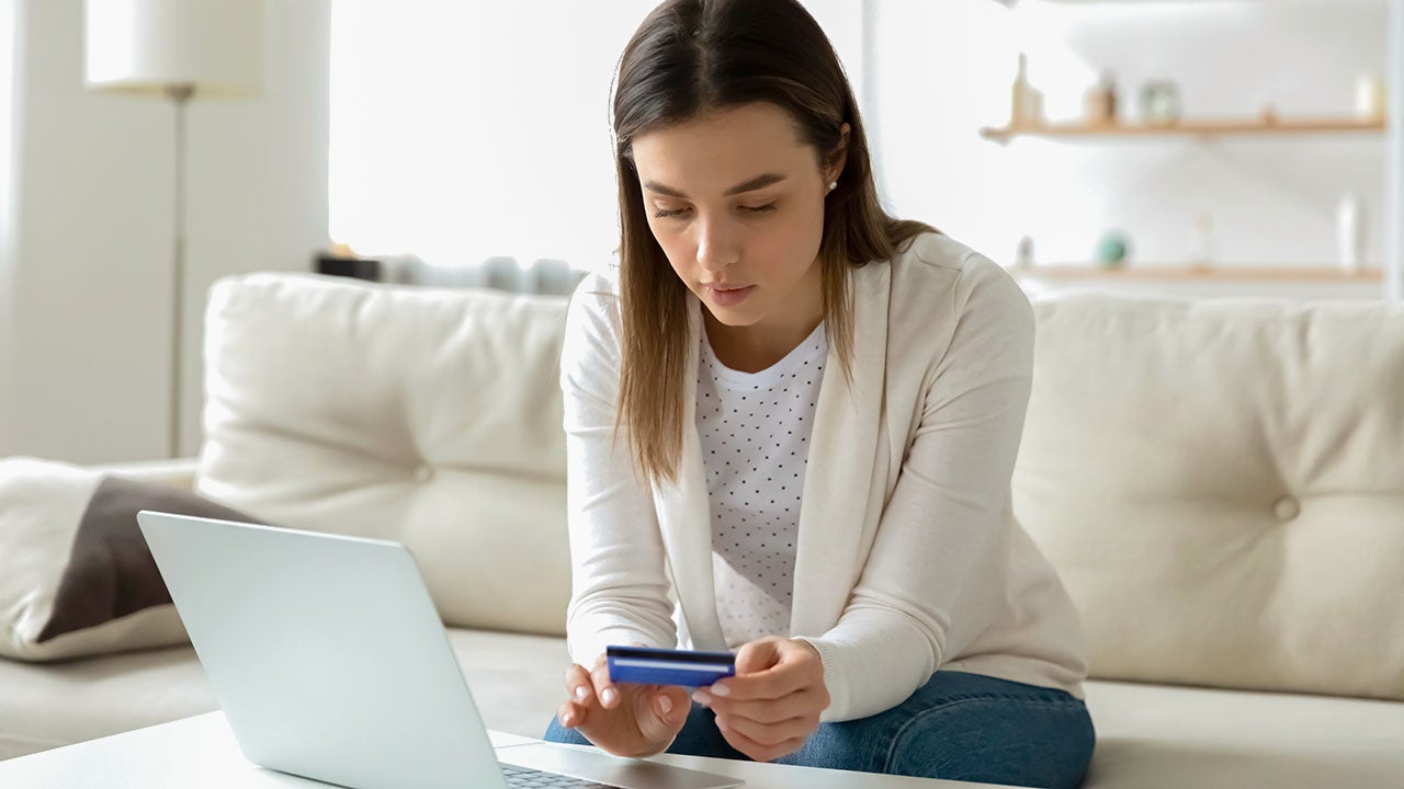 Focused young woman entering banking credit card information in computer application, making household payments online, booking flight tickets or hotel, purchasing goods or confirming transaction.