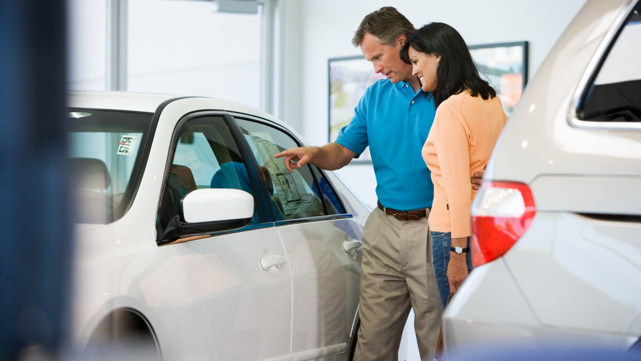 Man and woman browsing white car's sticker price in dealership