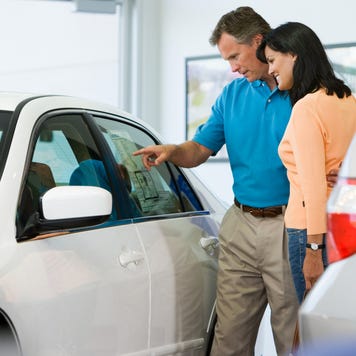 Man and woman browsing white car's sticker price in dealership