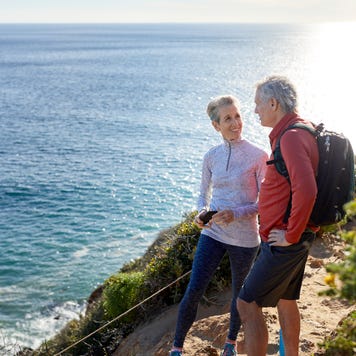 Couple talking while standing on cliff by sea during sunny day