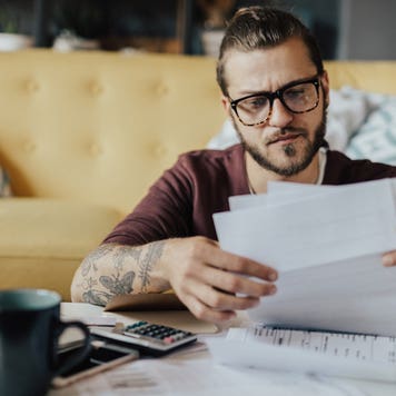 man working on his finances at home with laptop and papers