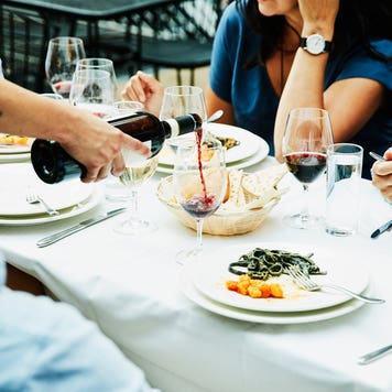 Server pouring wine for friends having a meal on restaurant patio