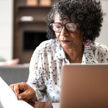 senior woman looking at paperwork in front of a computer
