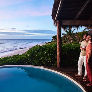 couple standing poolside watching sunrise at luxury tropical villa overlooking beach and ocean