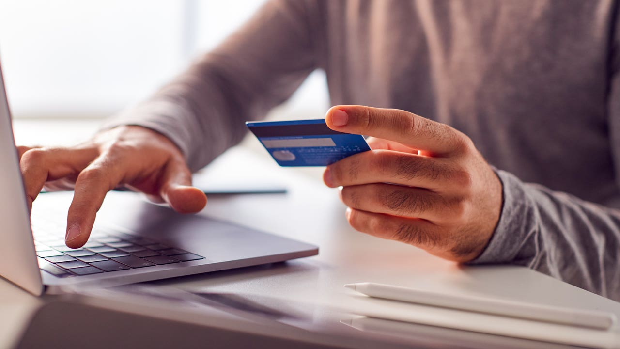 close up of hands holding a credit card and typing on computer