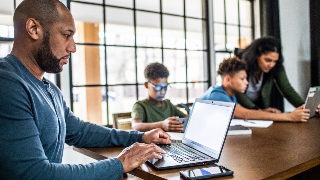Father on laptop in residential kitchen with family in background