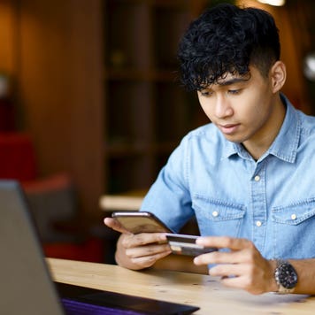 young man holding a credit card and looking at his phone