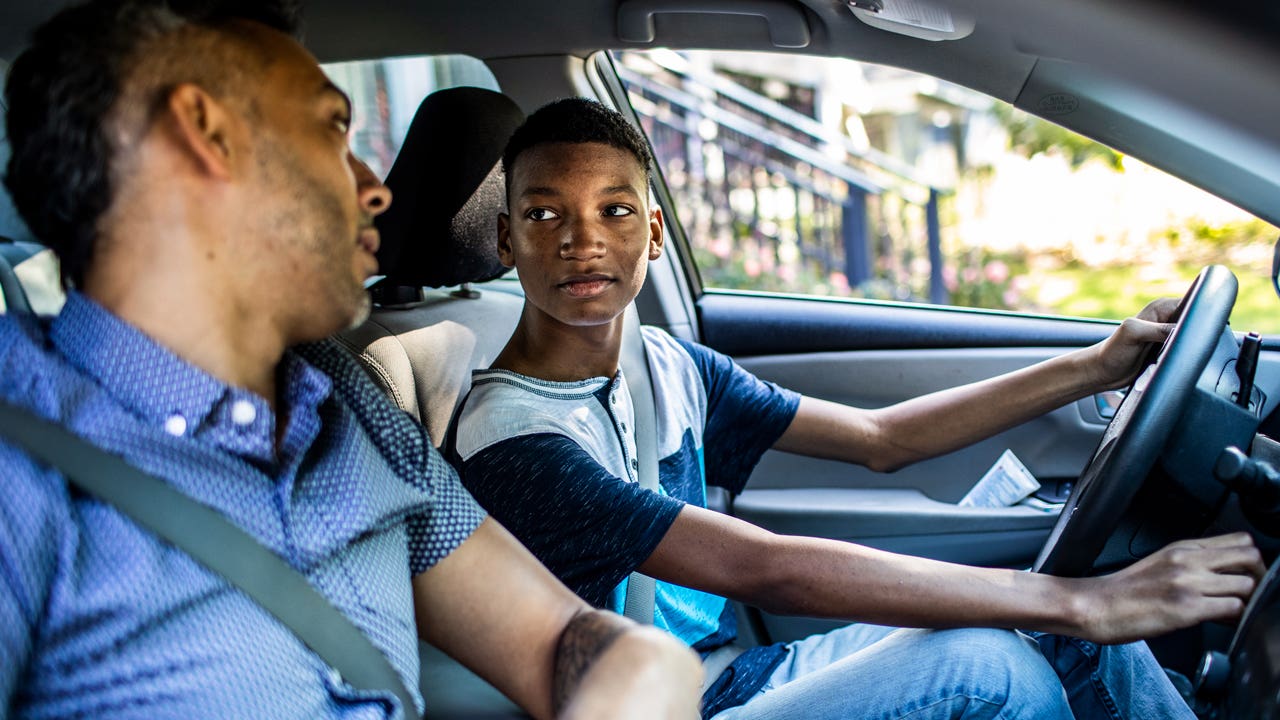 teenage son driving with his father