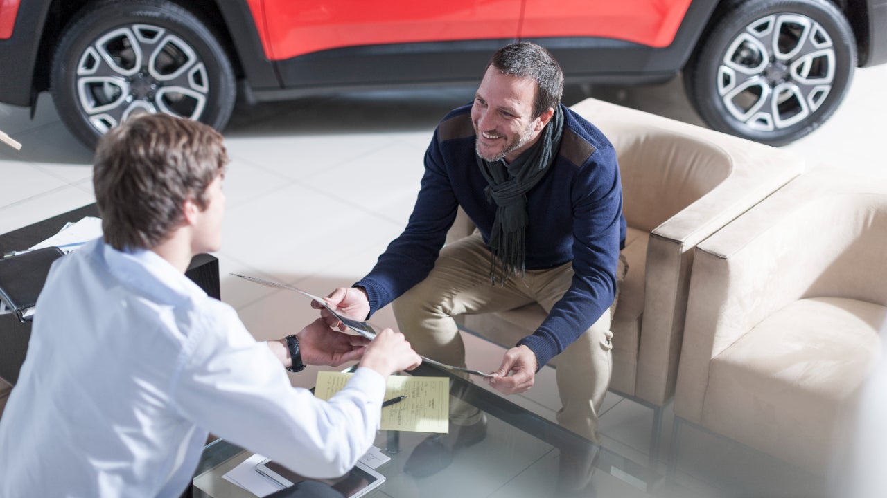 Man sitting at table in car dealership reviewing options with salesperson