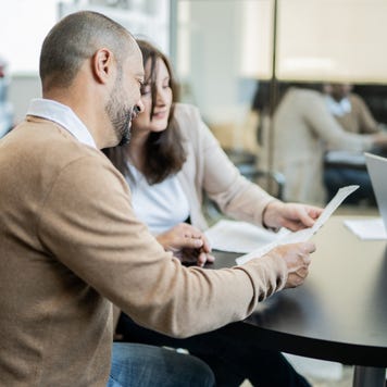 Man and woman sitting in dealership reviewing papers at a table across from salesperson who is out of frame