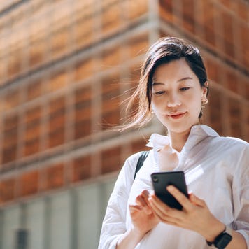 Well-dressed woman in front of big building smiling down at phone