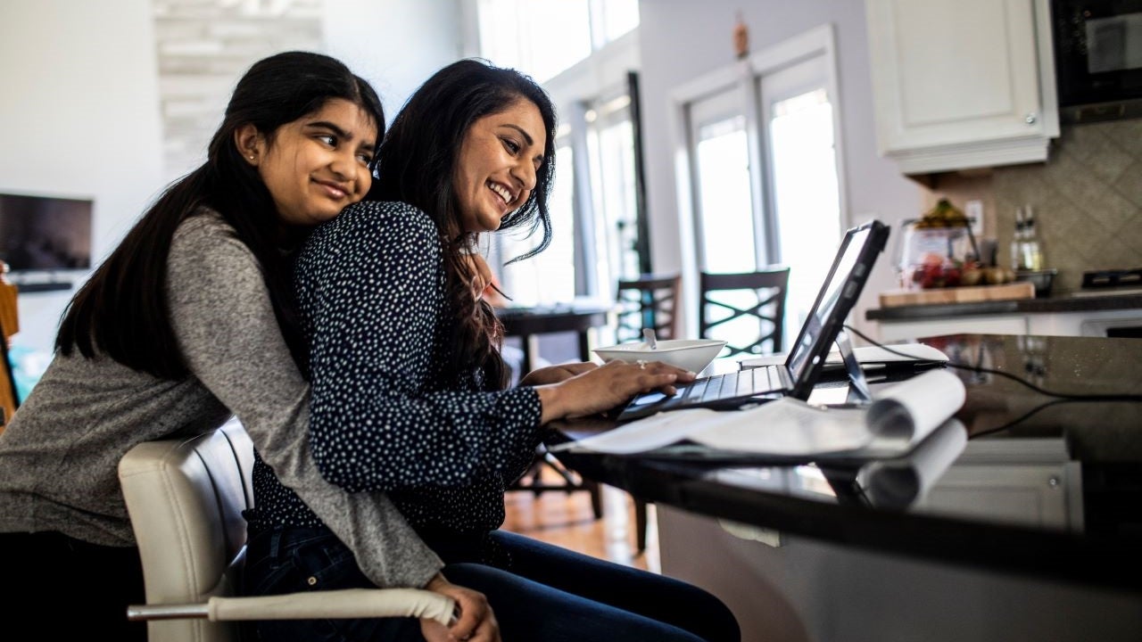 Two Southeast Asian women work on a laptop together.