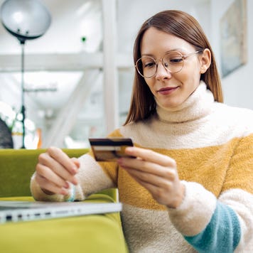 young woman looking at her credit card and working on her laptop
