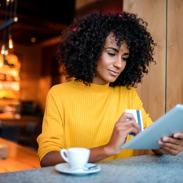 woman in a cafe using a digital tablet and holding her credit card