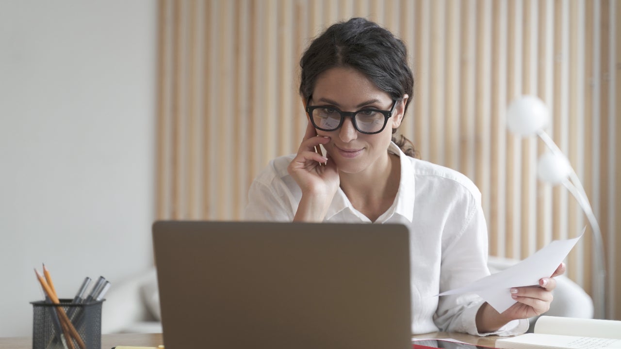 A woman smiles while looking at her laptop computer