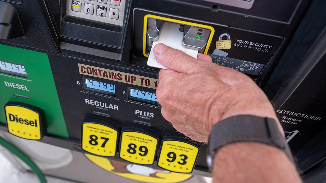 Man inserting credit card into gas pump with high prices