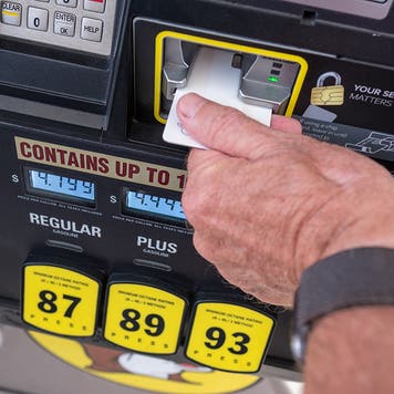 Man inserting credit card into gas pump with high prices