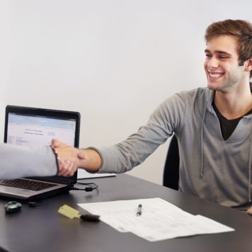 Couple sitting at desk across from car salesperson, smiling and shaking hands