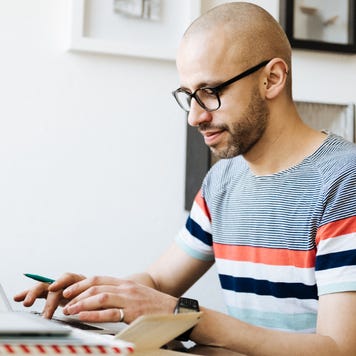 Man in a striped shirt smiling and typing on laptop at home table