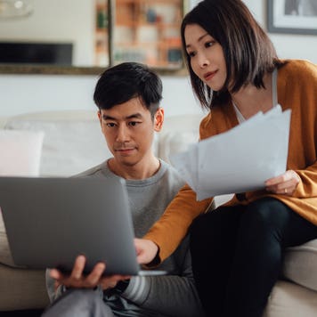 Serious looking young couple discussing over financial bills while using laptop in living room.