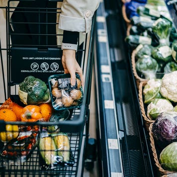a close up shot of person filling up a grocery cart next to produce section at a store