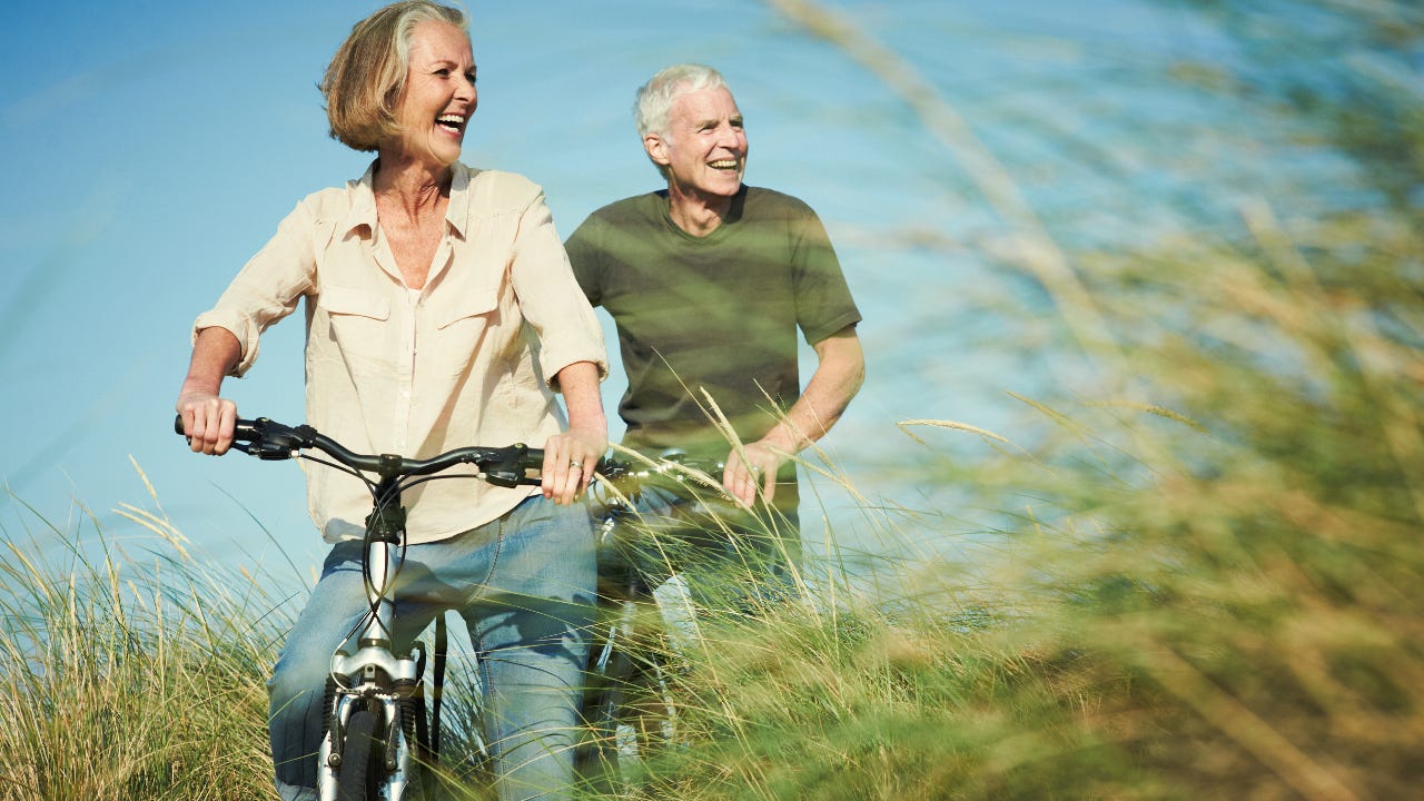 A retired couple rides bikes through a field.