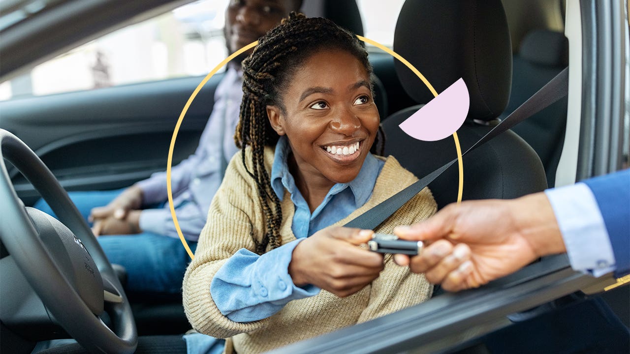 A young Black woman smiling as she takes a key while sitting in the driver's seat of a vehicle.