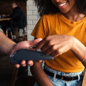 Smiling mixed race woman with afro happily paying for coffee at coffee shop