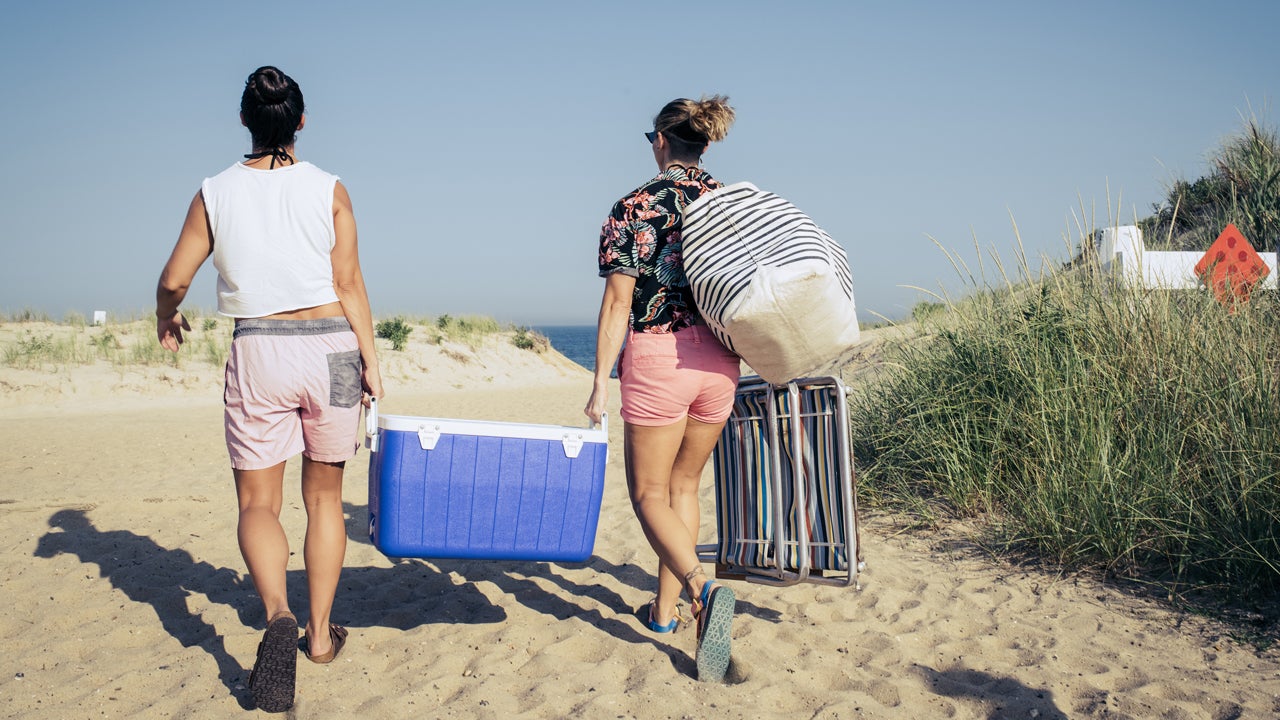 Two people carrying a blue cooler on the beach