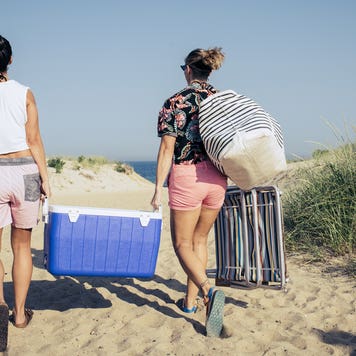 Two people carrying a blue cooler on the beach