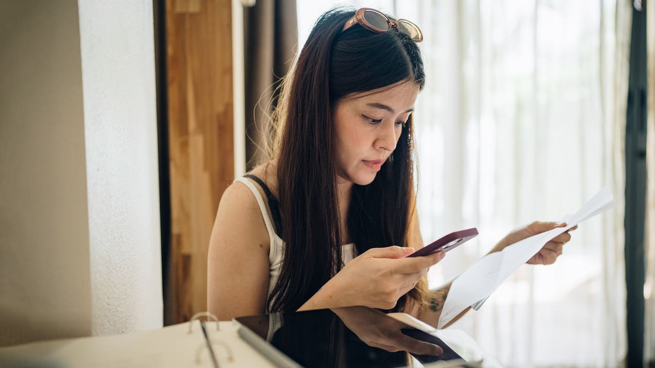 woman looking at her phone and bills