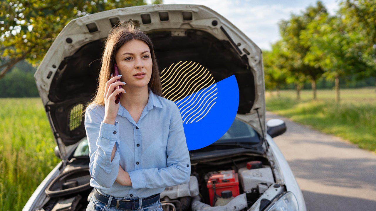A driver standing in front of their car pulled off to the side of the road with the hood up; they are on their phone