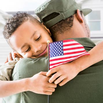 Soldier hugging patriotic son outside house