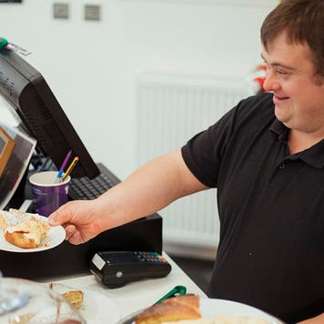 A man with Down syndrome is serving cake in a cafe where he works.