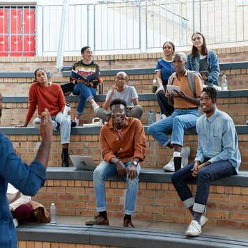 Young male professor teaching multi-ethnic students sitting on amphitheater steps at university campus