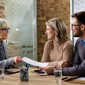 Happy senior agent giving her customer paperwork while having a meeting in the office.