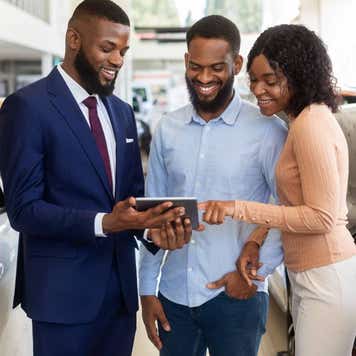 Dealership Center Manager Showing Vehicle Characteristics On Digital Tablet To Young Black Couple
