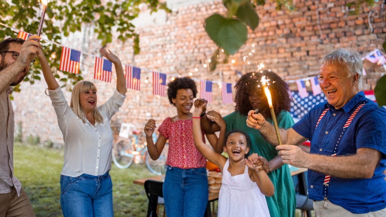 Multi-generation family waving sparklers outdoors on an American national holiday