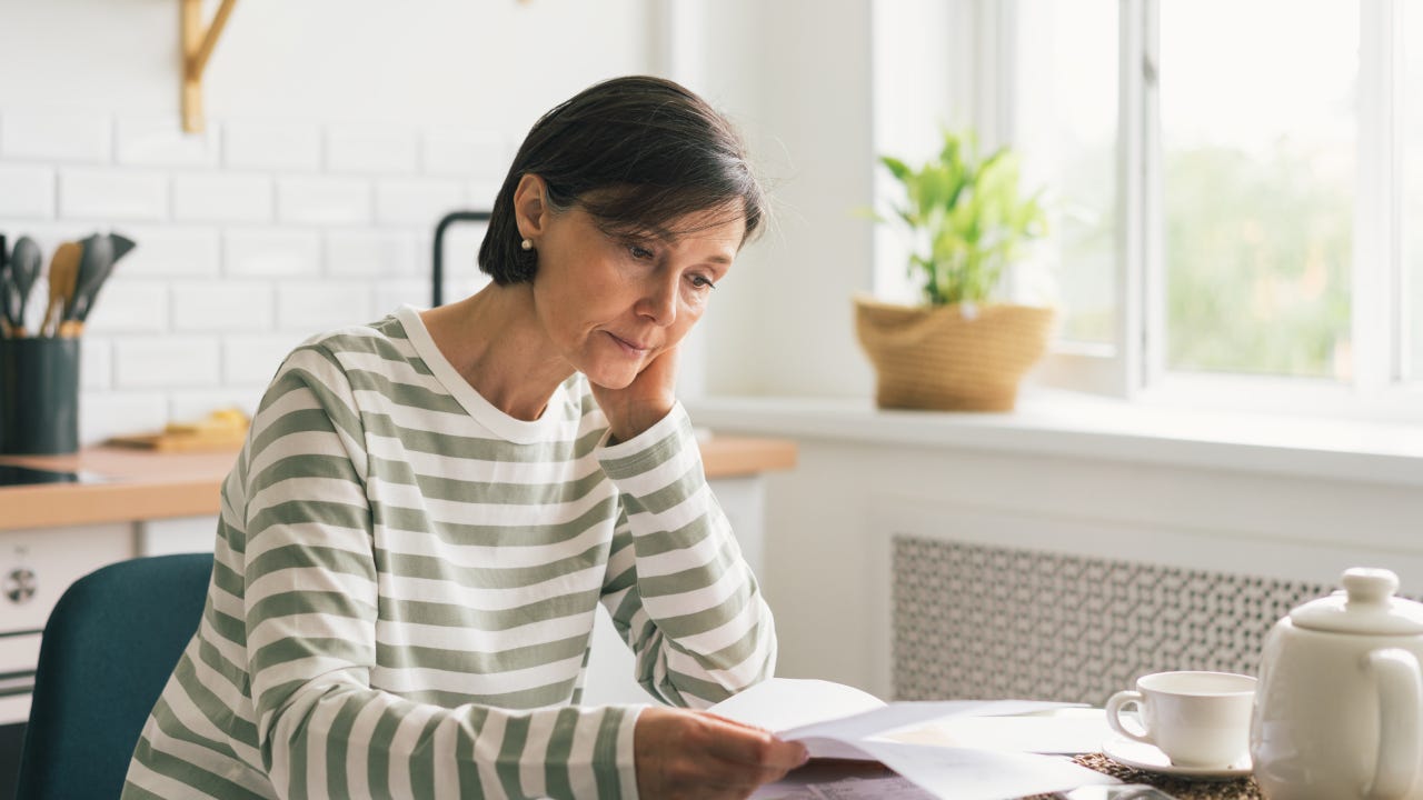 Upset woman thinking about high prices while looking at utilities, gas, electricity, rental charges, water bill due to inflation and crisis. Planning personal budget while sitting in kitchen. Weighing options on how to save money