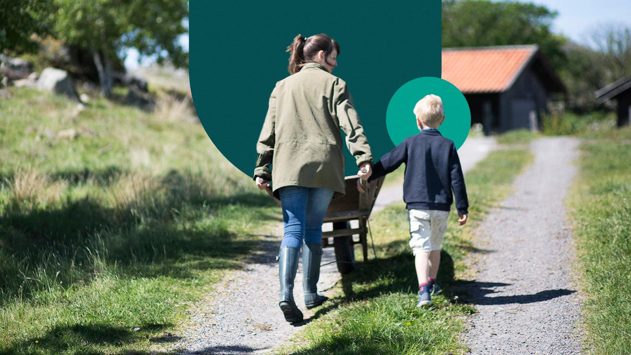 Woman holding a child's hand while steering a wheel barrel